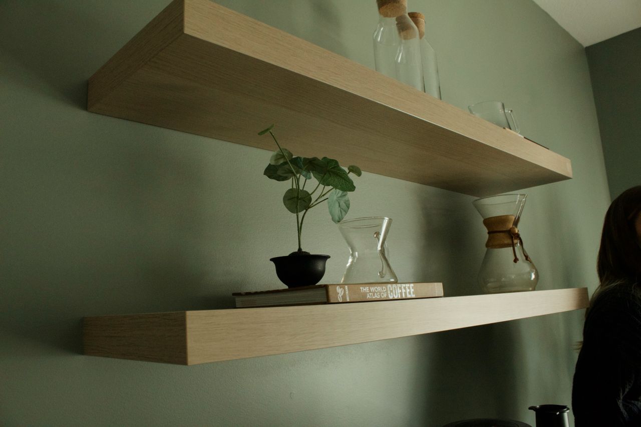 Home Chic floating shelves with books, decorative plants, and carafes on a green wall.